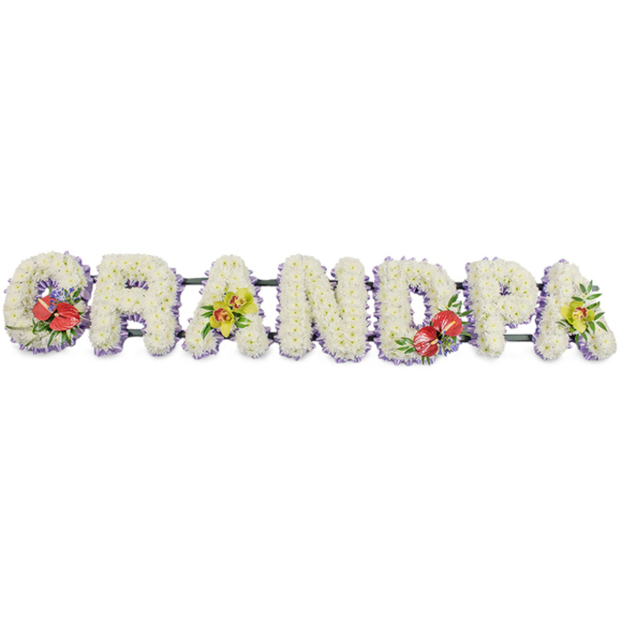 A bespoke sympathy tribute spells out the word "GRANDPA" in large, block capitals, the letters arranged in a straight horizontal line as if resting on a stand at the front of a funeral or memorial service. Each letter is fully padded with small white chrysanthemums, so closely packed that their petals blend into a continuous, textured surface resembling a soft floral cushion, symbolising purity, peace, and the gentleness of cherished memories. Along the bottom edge of the letters runs a neat band of pale lilac ribbon, glimpsed just beneath the blooms, providing a subtle, cool-coloured outline that enhances the clarity of each shape without interrupting the calm field of white. The letters are supported on dark green bars, discreet yet strong, linking the arrangement together as one unified tribute. Carefully placed accent sprays introduce contrast and personality. On the "G" at the far left and the "D" towards the right, striking clusters of deep red anthuriums stand out, their heart-shaped, waxy spathes and yellow spadices framed by glossy green foliage and small supporting flowers. On the first "A" and the last "A", delicate yellow-green orchids are nestled among leaves, their refined forms and soft colouring adding a sense of enduring elegance. The background remains completely white, keeping the focus on the flowers and the name they lovingly form. Crafted in the style often requested by families in Honor Oak, Forest Hill, and nearby Brockley, this "GRANDPA" tribute offers a dignified, clearly personal way to honour a grandfather's life, expressing love, respect, and remembrance through careful floristry and thoughtful design.