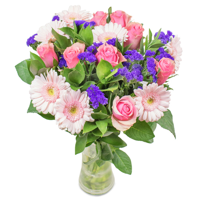 Set against a bright, neutral background, this captivating Honor Oak floral arrangement features an elegant gathering of approximately seven to nine roses in the softest to most vibrant pinks, each rose blooming in classic spirals or shyly folded just beyond bud-each form a celebration of subtlety. Around five to seven Gerbera daisies, their heads round and petals gently lighter at the centre, cluster among the roses, adding fresh, cheerful volume to the design. Scattered through this harmonious collection are bold, purple clusters-statice or limonium-providing a striking textural counterpoint and anchoring the bouquet in rich, natural hues found near the ancient trees of One Tree Hill. The base brims with deep, glossy greenery, evoking the lushness of Honor Oak's parks in spring. The entire arrangement is presented in a clear glass vase, with stems visible and water sparkling, accentuating the authenticity and freshness at the heart of our community. An ideal option for birthdays, anniversaries, or Mother's Day, this bouquet is a sophisticated yet joyful expression of celebration and enduring affection-perfect for making any moment in SE23 extraordinary.